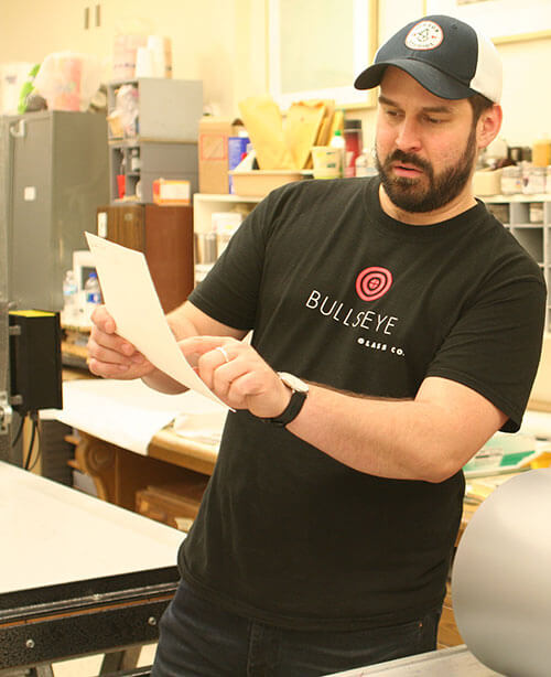 Artist Matthew Day Perez stands in the studio, pointing to a paper in his hand.